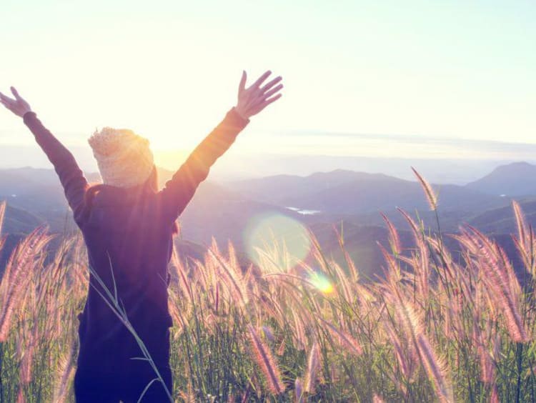 woman with arms raised in an open field