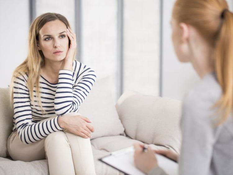 Young trauma counselor sits across beautiful woman in striped top 