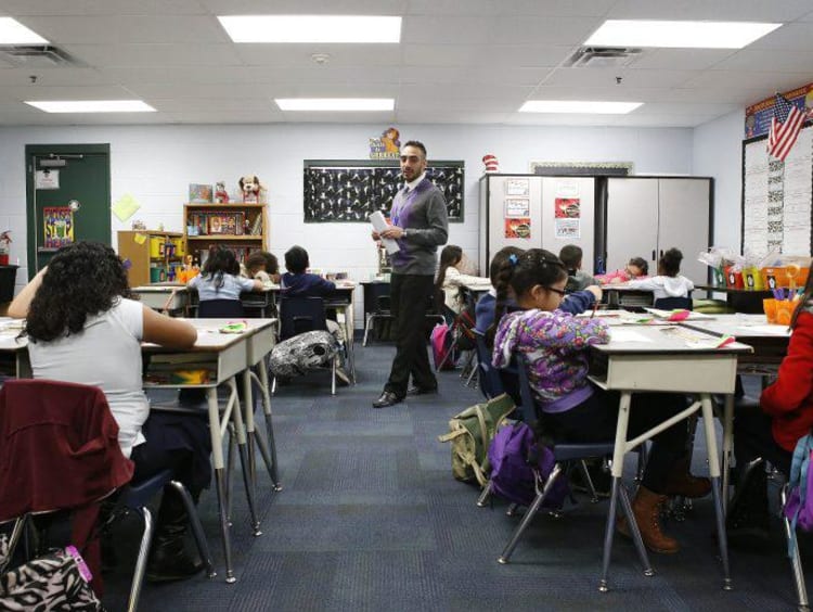 Hispanic male teacher paces classroom while students work