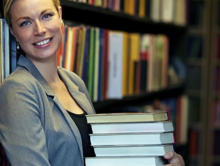 Attractive blonde woman holds stack of books in library