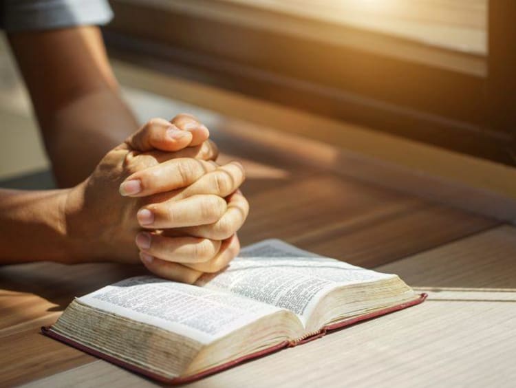 Man praying with his hands over a Bible