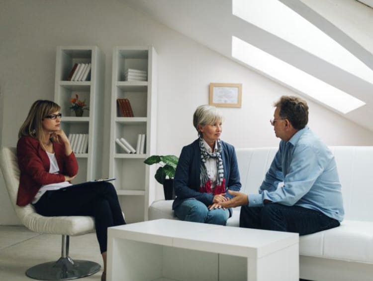 Female counselor observes older couple talking to each other face to face on white couch