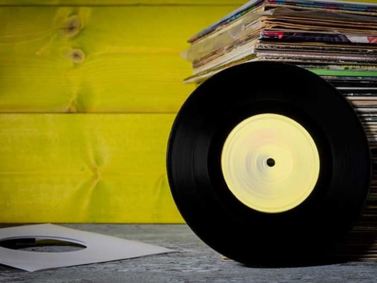 Yellow wall with table of stacked vinyl sleeves and a vinyl leaning against it