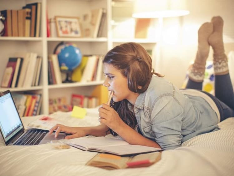 student doing homework on her bed