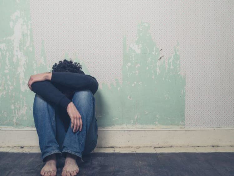 Man sits curled up next to a wall with head to knees