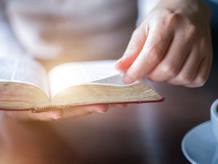 A hand turning a page in a Bible