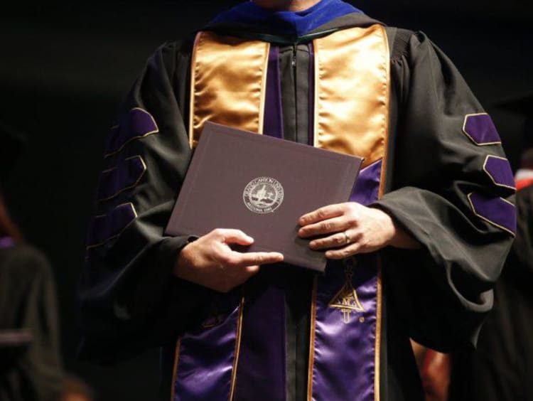 Doctoral student in graduation gown holds GCU diploma folder