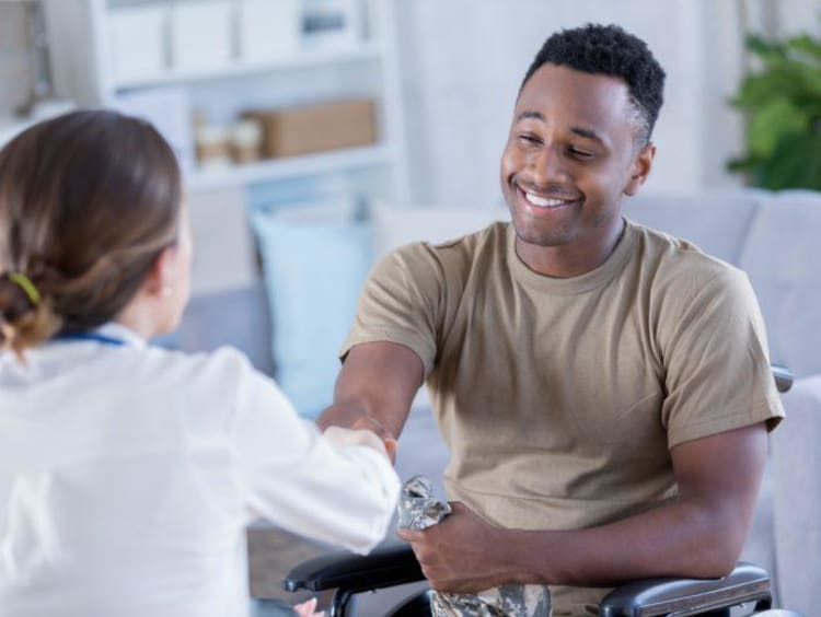 Female doctor shakes hand of African-American male patient who is smiling in wheel chair