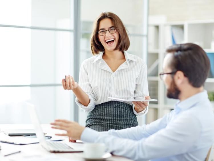 Woman laughs in an open office space while a man sits at a desk