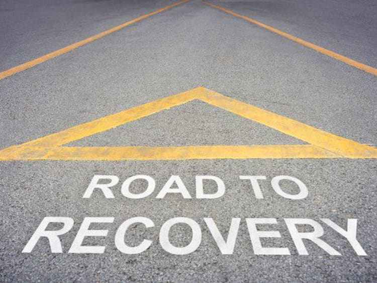 Yellow upright triangle above road to recovery lettering on a road