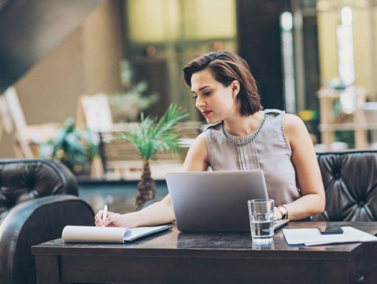 woman writing at a desk in front of her laptop