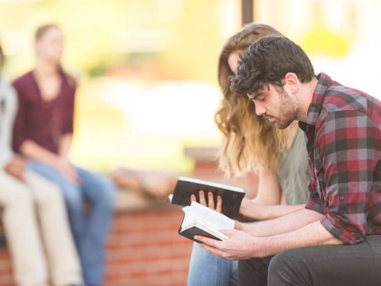 two people reading a book outside