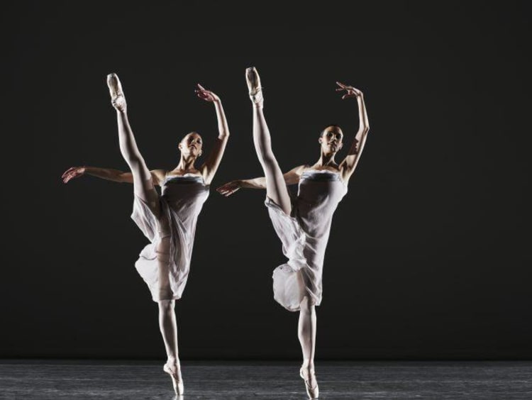 Two ballerinas dancing on stage, legs raised