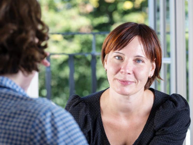 Woman with short red hair breaks a small smile facing a man with longer curly hair