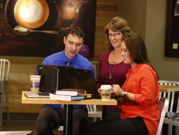 Group of adults gather around a laptop to look at it