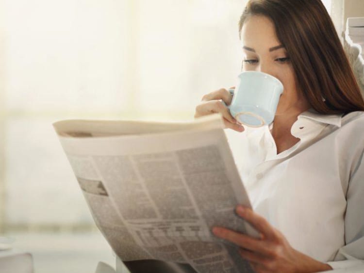 girl reading newspaper and sipping out of a mug