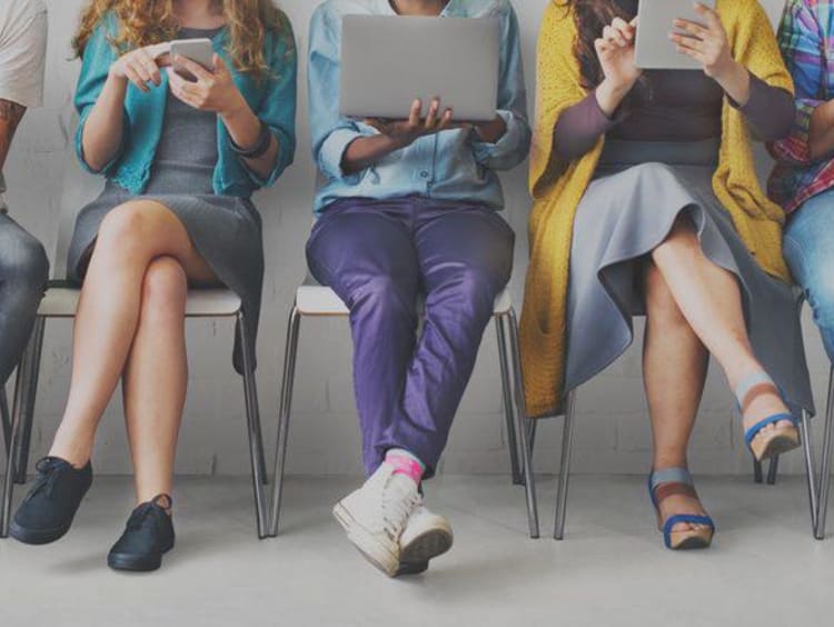 Front view of millennials sit in a row using phones and tablets