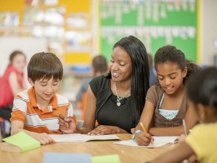 female teacher helping two young students in classroom