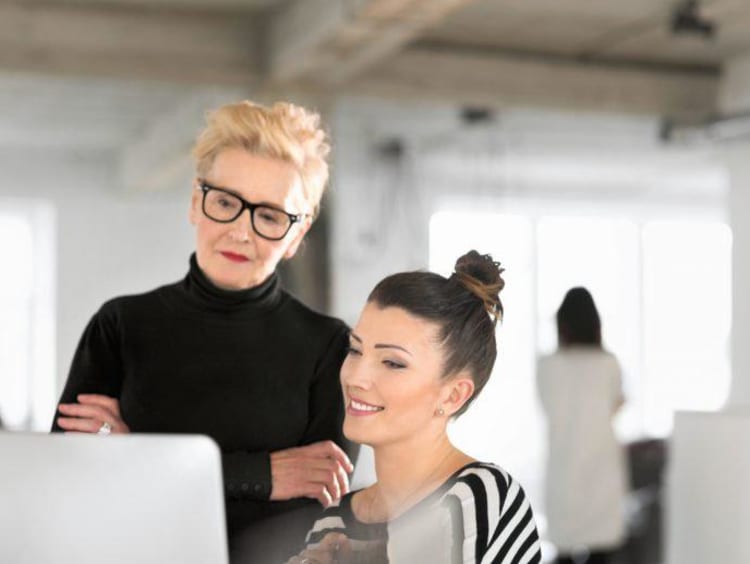 A woman at a computer with an older woman helping her