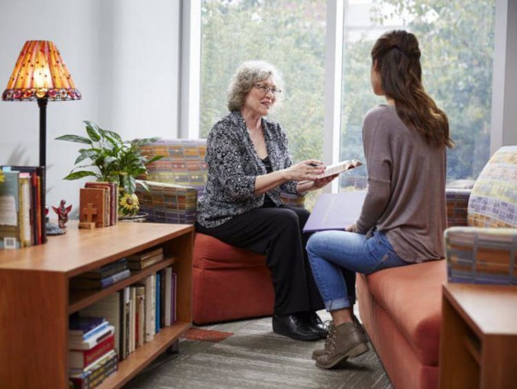 Older woman shares Bible reference with younger female sitting across from her