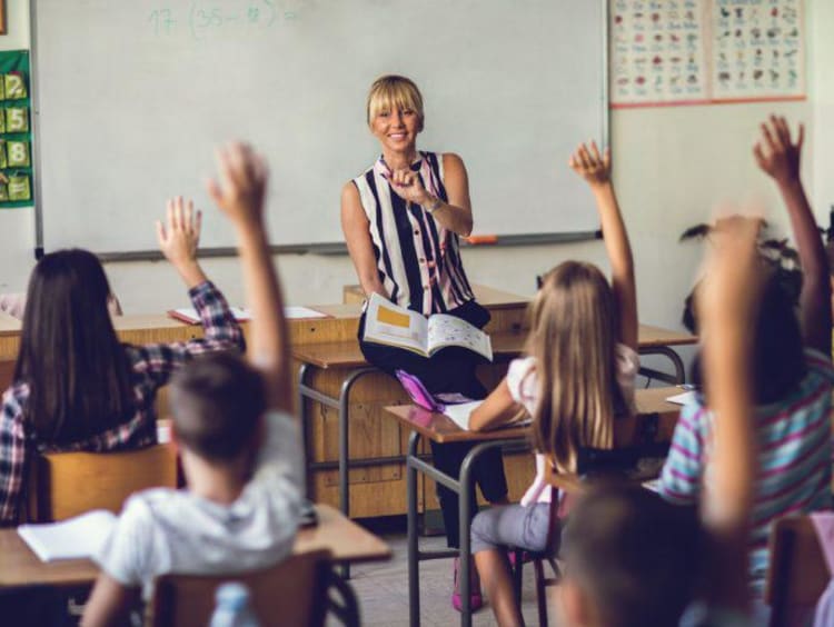 Teacher points out student in classroom of raised hands