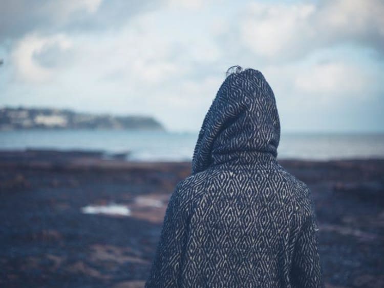 Back of hooded individual looking out at a barren landscape