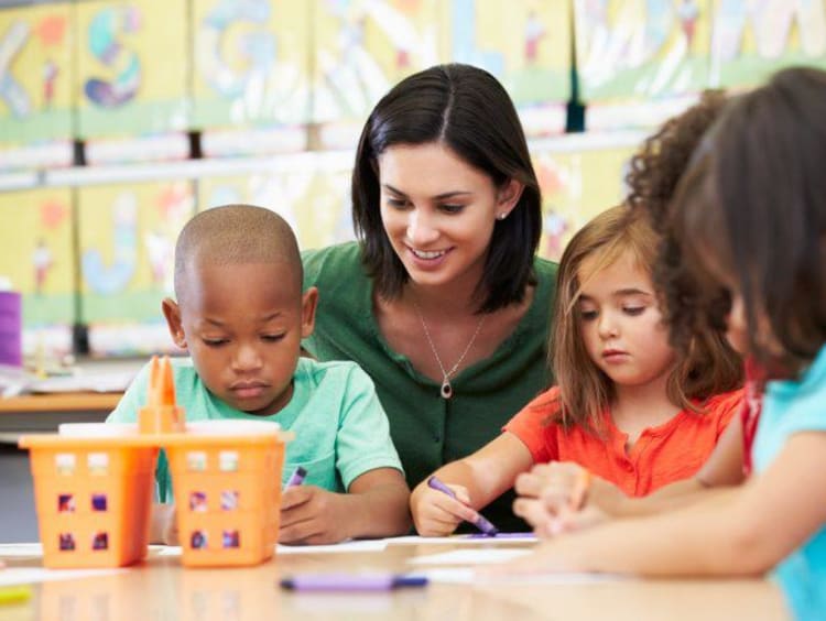 Elementary art teacher observes three kids coloring at a table