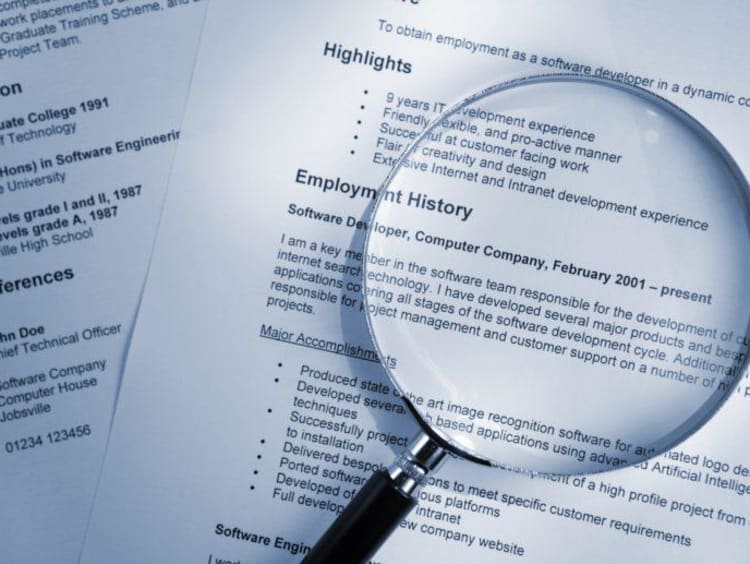 A stack of resumes with a magnifying glass on top