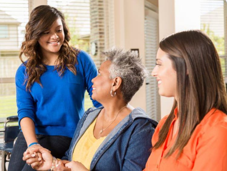 Young woman smiles holding hand of older woman with a third woman seated next to her