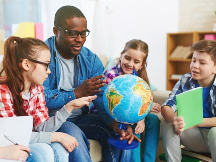 teacher holding globe and surrounded by young students