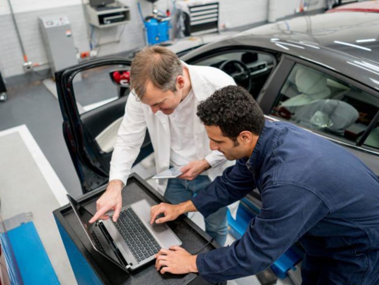 Man working on a computer by a car