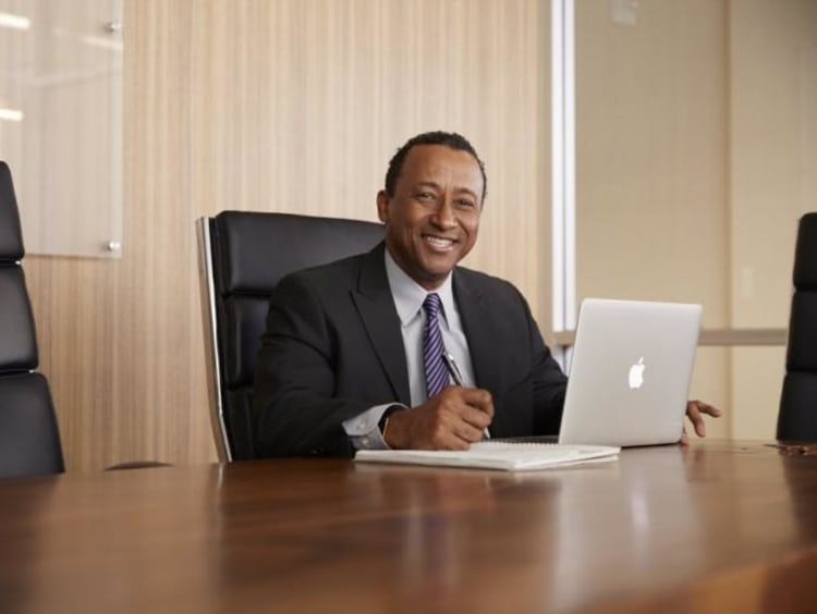 Smiling man in suit and tie sits in conference room with laptop open