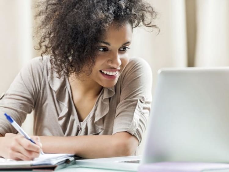 girl looking at computer and writing in a notebook