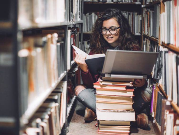 A female student researching in a library surrounded by books