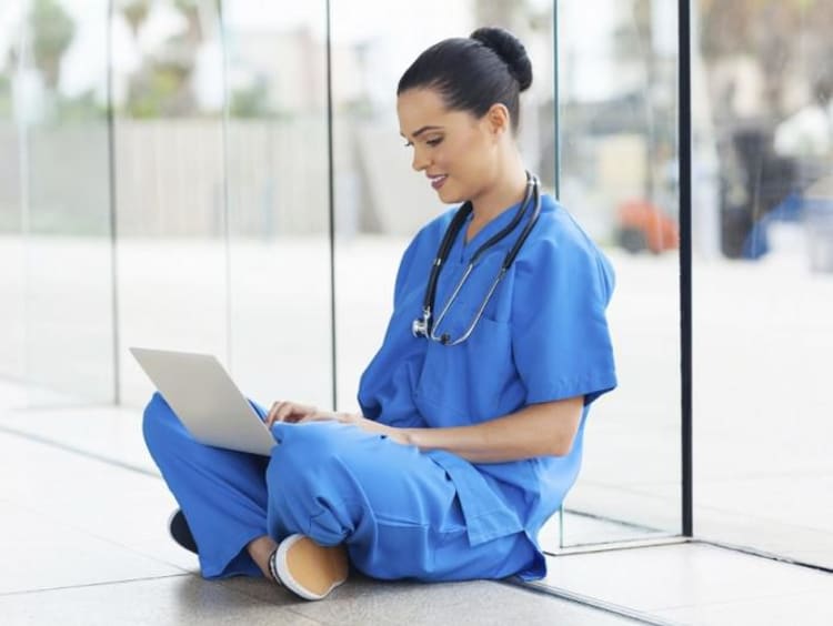 nurse sitting on floor typing on a laptop