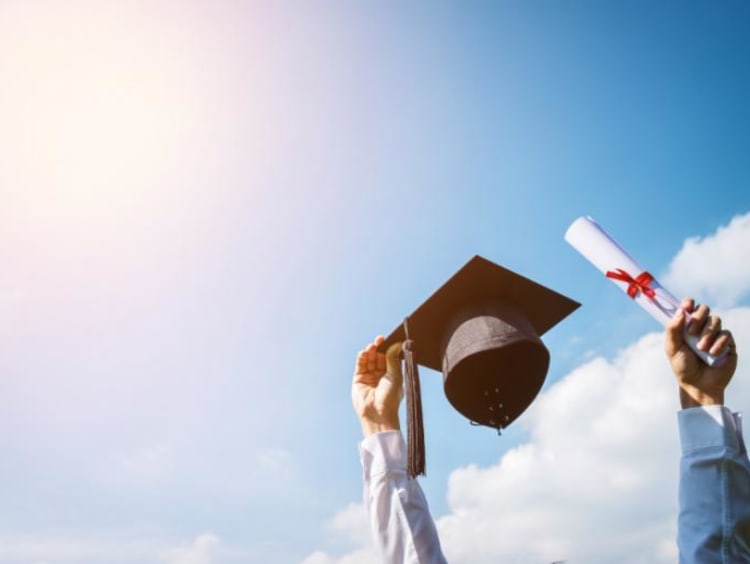 Man holding cap and diploma up in the sky