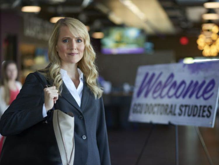 Blonde woman in professional clothing stands at entrance for doctoral studies mixer