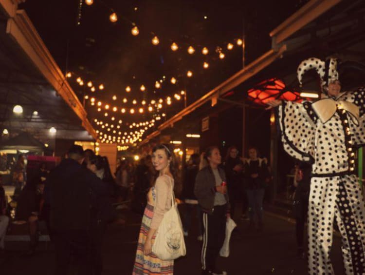 Kaitlyn stands in the middle of a busy Melbourne marketplace at night 