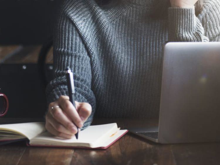 person writing in a journal and on a computer