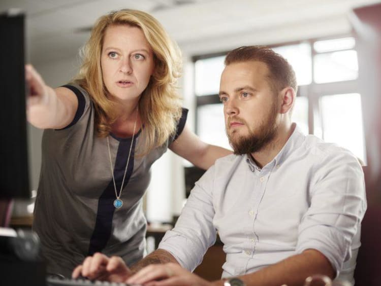 Woman stands next to seated male in white shirt and points to item on screen