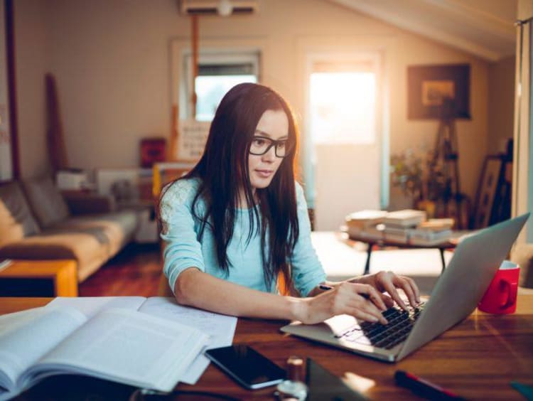 Woman works on laptop at a table in living room