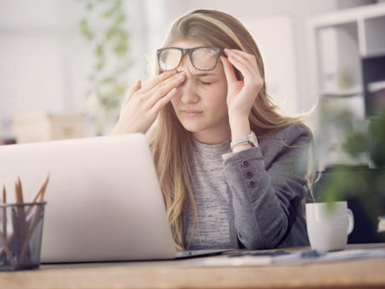 girl rubbing eyes while sitting in front of a computer