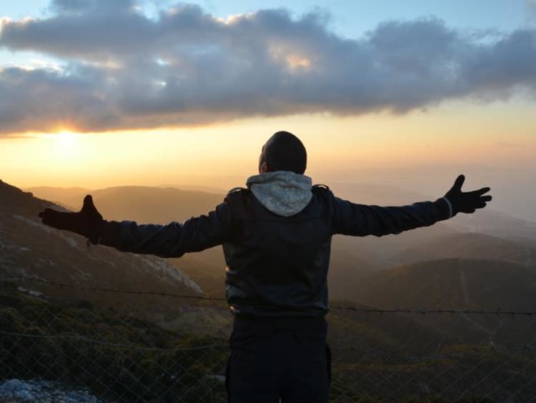 A man spreading his arms at the top of a mountain at sunset