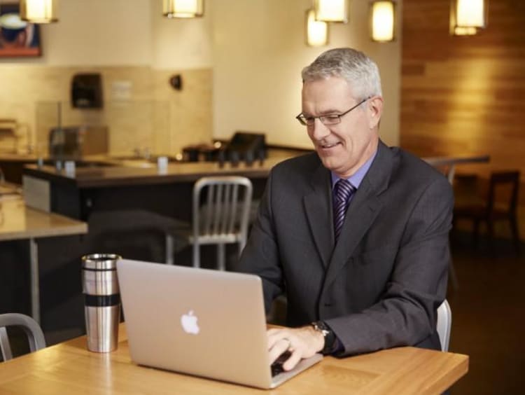 Older businessman uses laptop in empty coffee shop