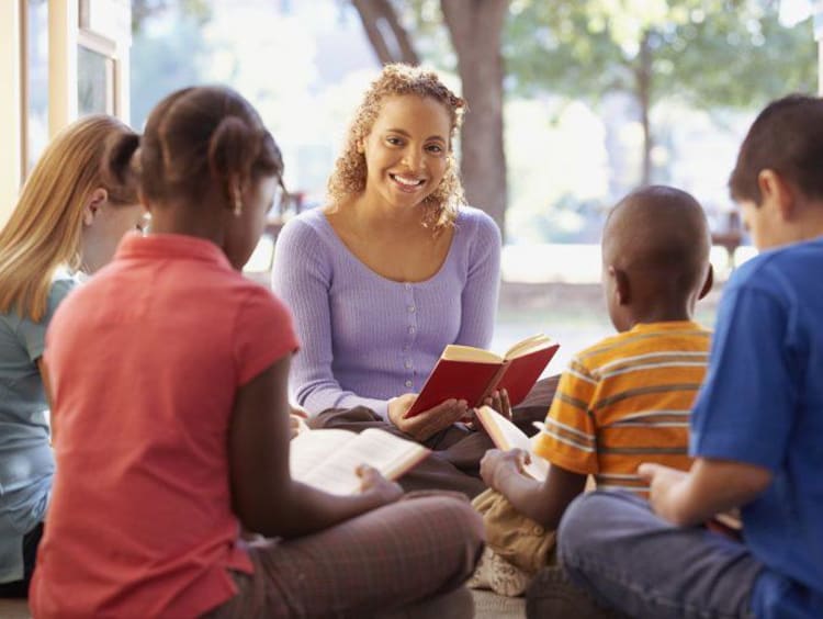 Teacher reads aloud to students sitting on the ground