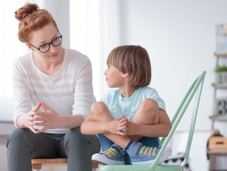 Female behavioral health counselor sits with young boy in play room