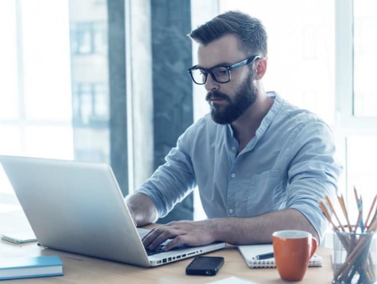 Bearded male sits at desk and uses laptop