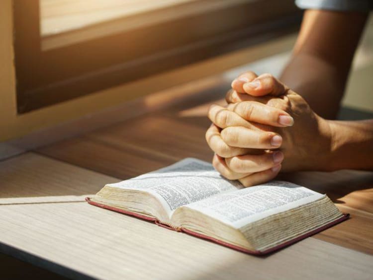 man with folded hands praying on a bible