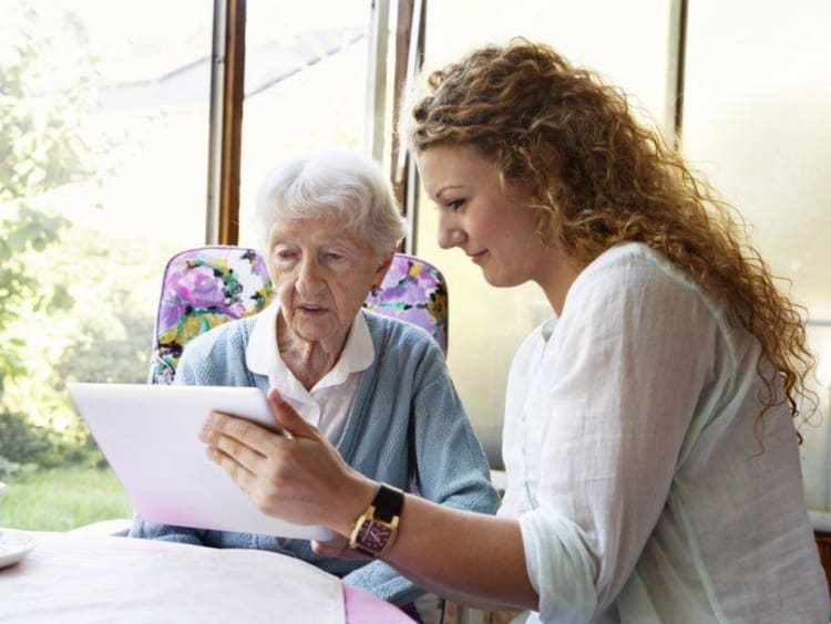 Woman with long curly hair shows elderly woman something on tablet