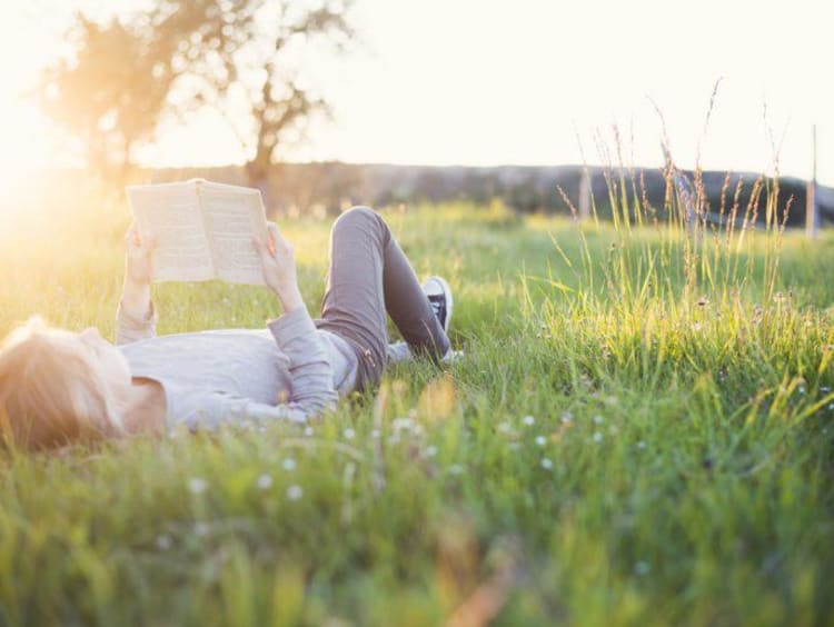 Woman lays in the grass and reads a book